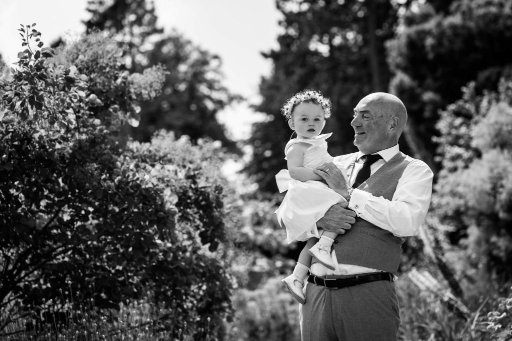father of the bride holding up the flower girl in the gardens