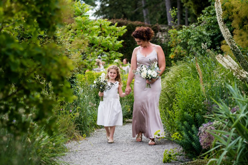 bridesmaid and flower girl walking down a path towards the ceremony