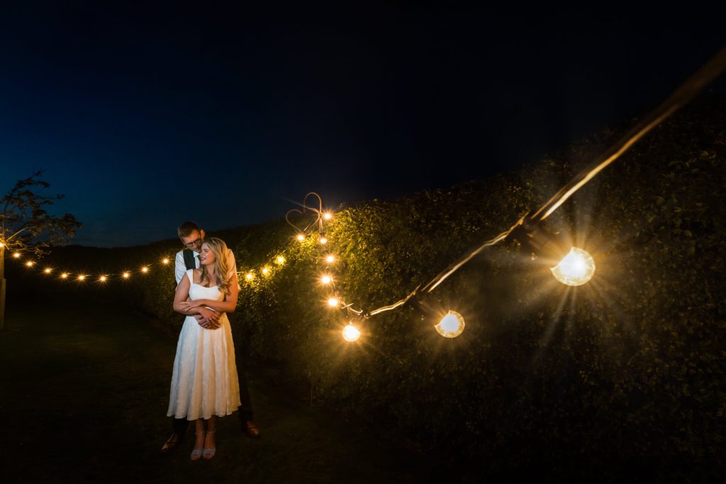 wedding couple embracing by some fairy light at night at Woolas Barn