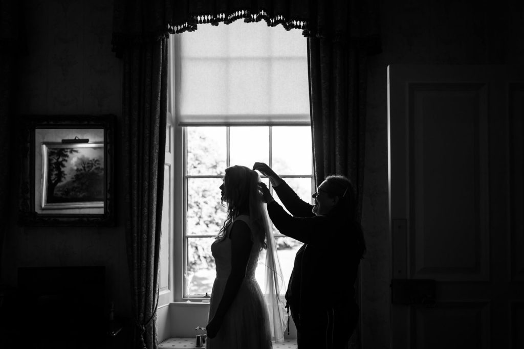 silhouette of a bride in front of a window having her veil put on