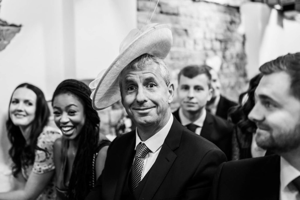 male wedding guest wearing a woman's hat and guests laughing