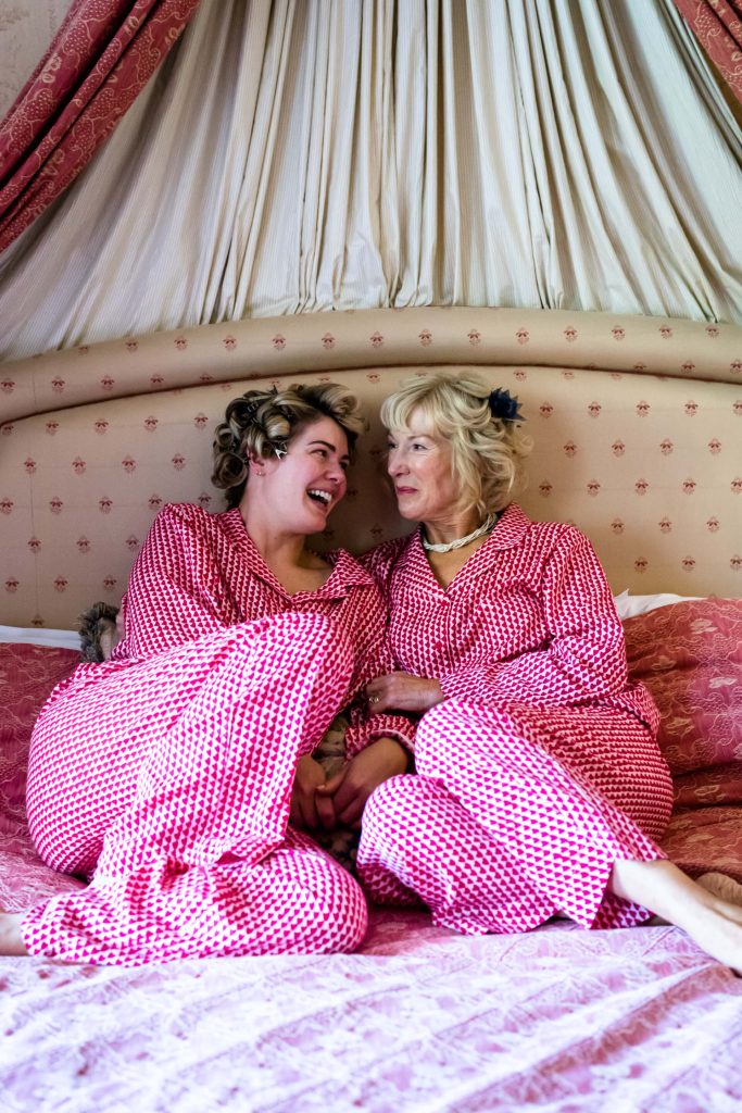 bride and her mum sitting on a bed an laughing together