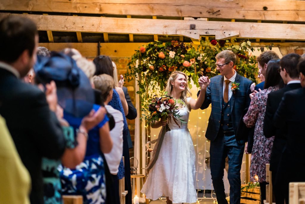 bride and groom cheer as they walk down the aisle at Woolas Barn
