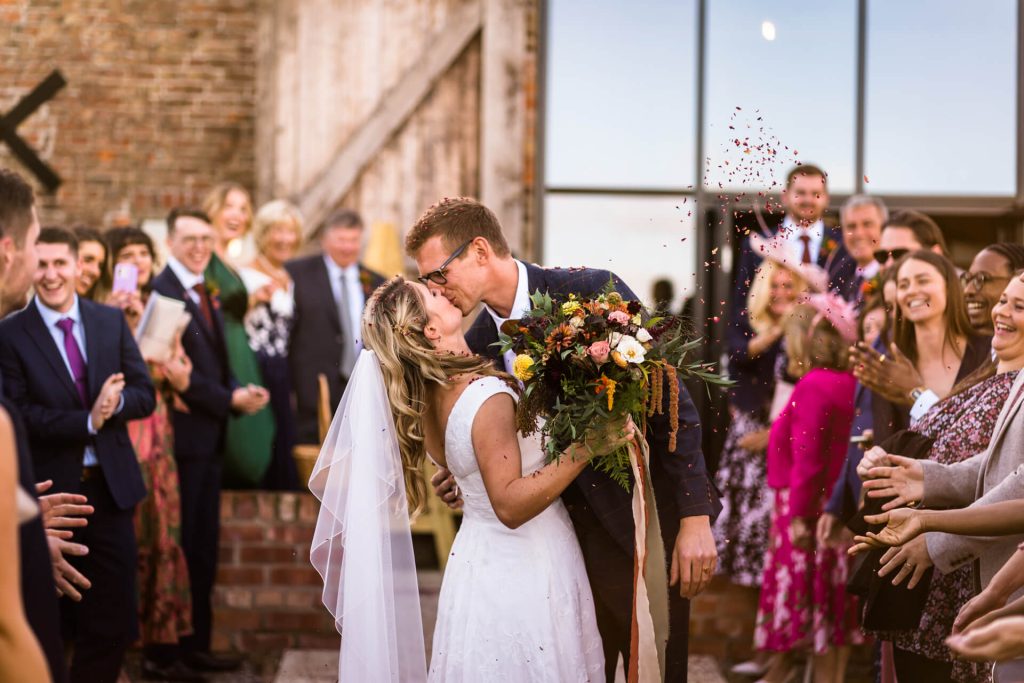 bride and groom kiss in the middle of the confetti tunnel at Woolas Barn