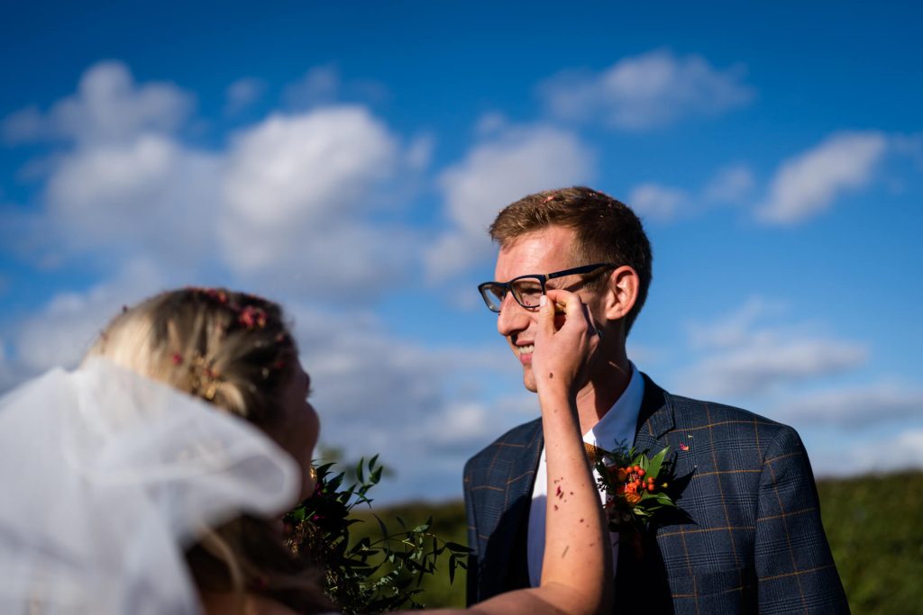 bride reaches to get the confetti out from behind the grooms glasses