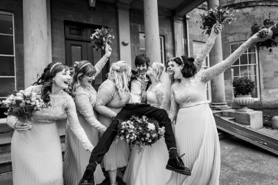 bride kisses the groom as he is picked up by all the bridesmaids at Rudding Park