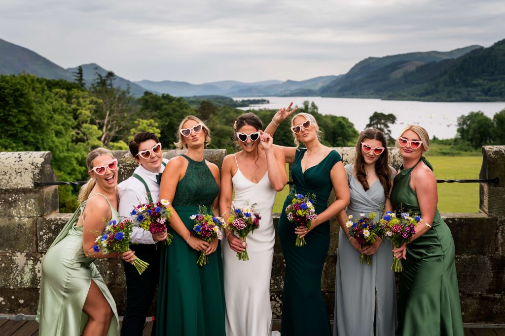 Bridal party posing with sunglasses and bouquets, on a balcony at Armathwaite Hall