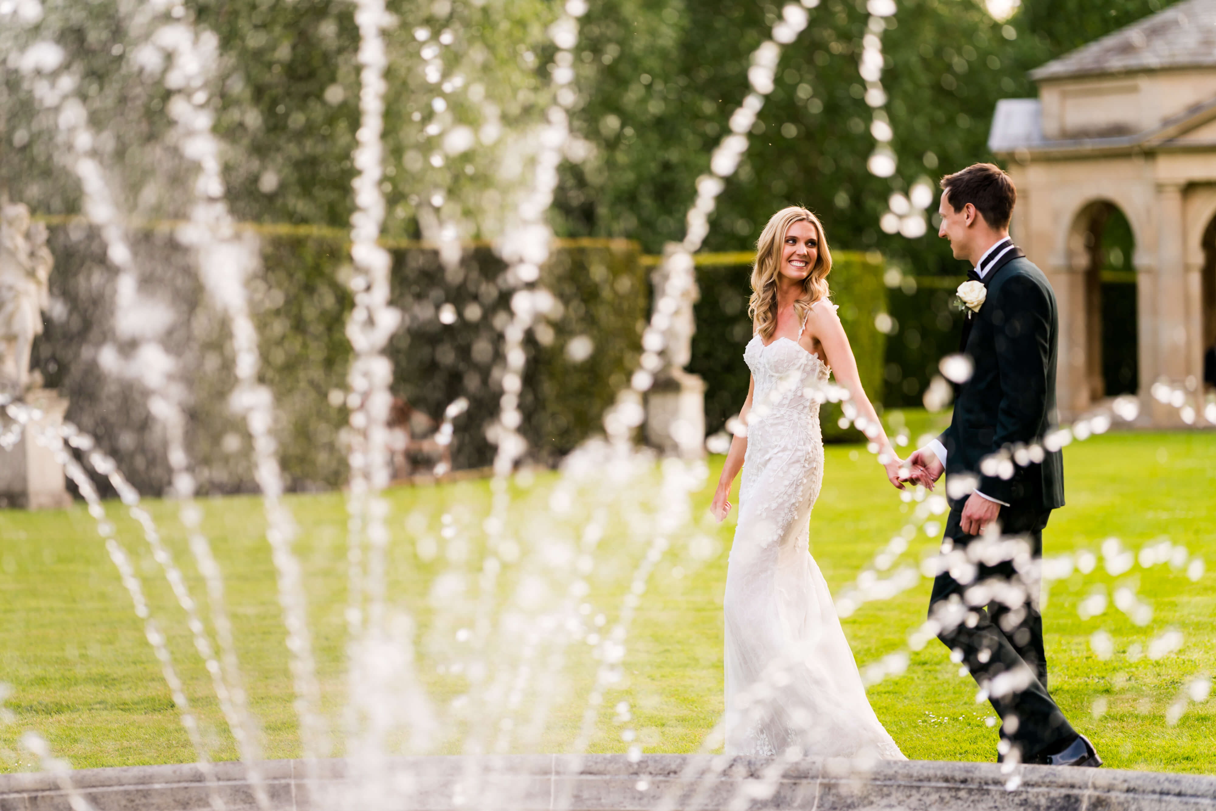 Bride and groom holding hands near a fountain at The Orangery at Settrington