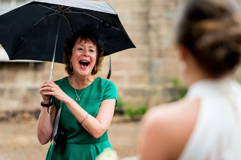 Woman with umbrella laughing at the bride