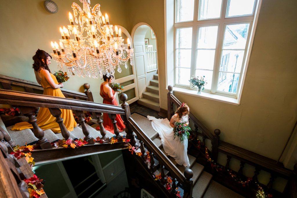 Bridal party descending staircase with elegant chandelier.