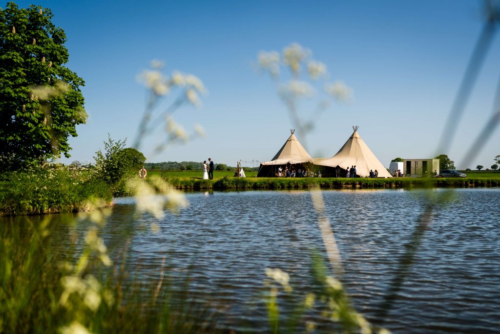 Outdoor wedding with tipi tents by lakeside at Low Osgoodby Grange