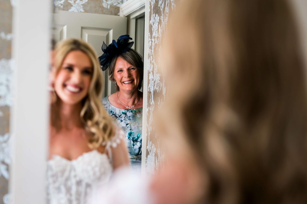 Bride and mother smiling, reflection in mirror.