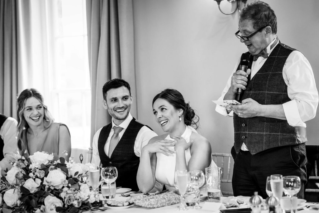 Wedding toast with joyful bride, groom, and guests in black and white.