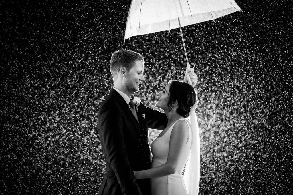 Bride and groom sharing moment under umbrella in rain