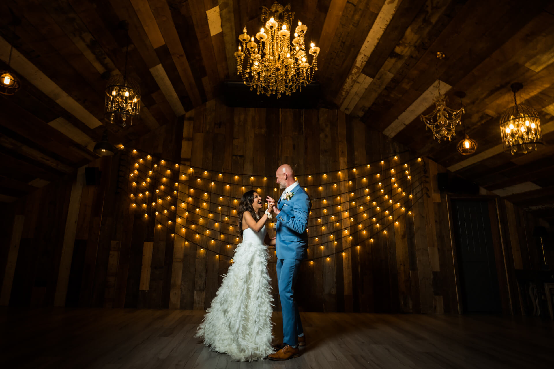 Couple dancing at rustic wedding venue with chandeliers.