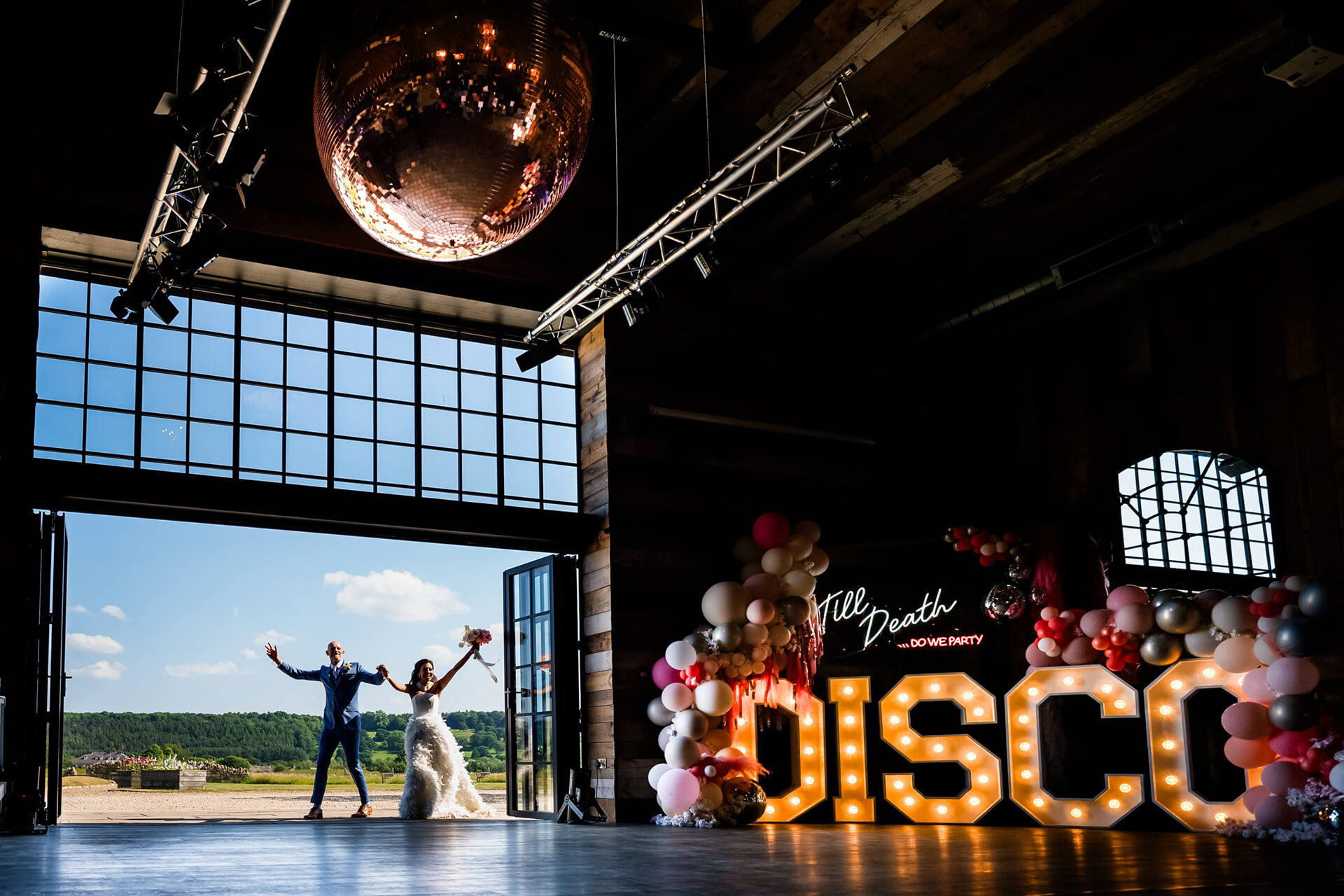 Wedding couple dancing under disco sign in rustic venue.