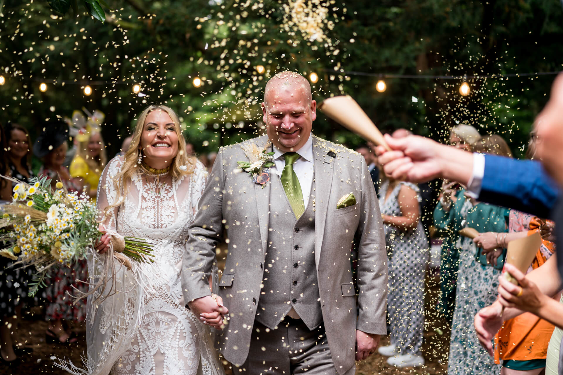 Bride and groom smiling with confetti at forest wedding.