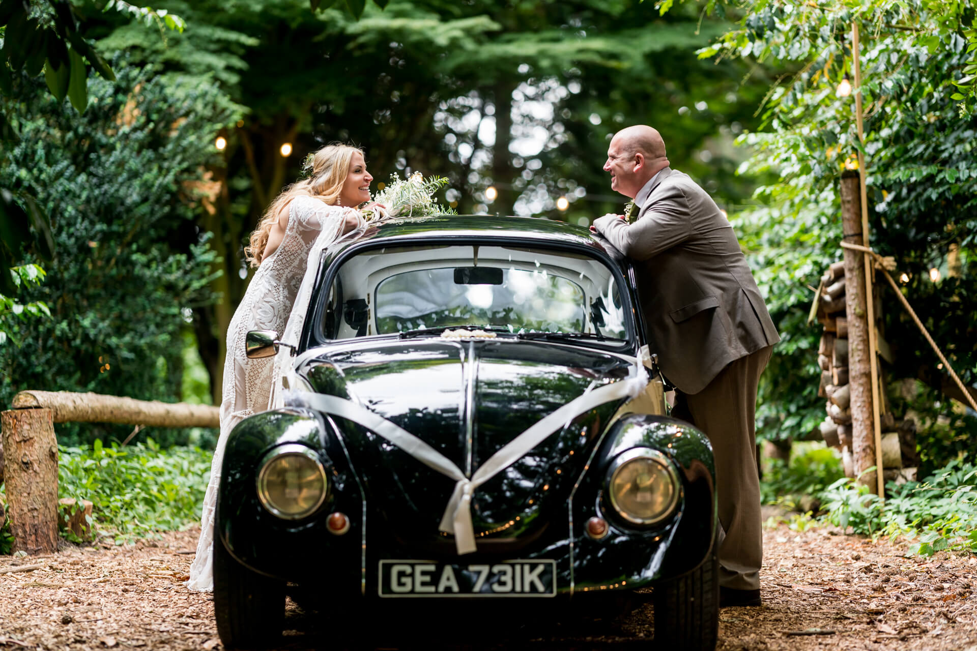 Bride and groom with vintage wedding car in forest.