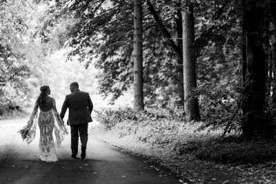 Couple walking hand in hand in wooded area.