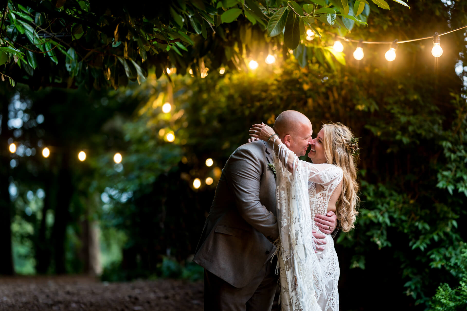 Couple embracing at outdoor wedding with string lights at Hazlewood Castle