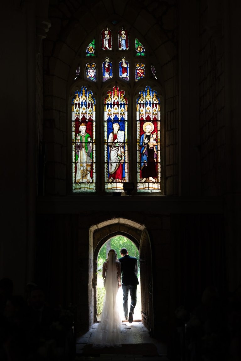 Silhouette of couple as they leave through the church archway, stained glass window, wedding ceremony