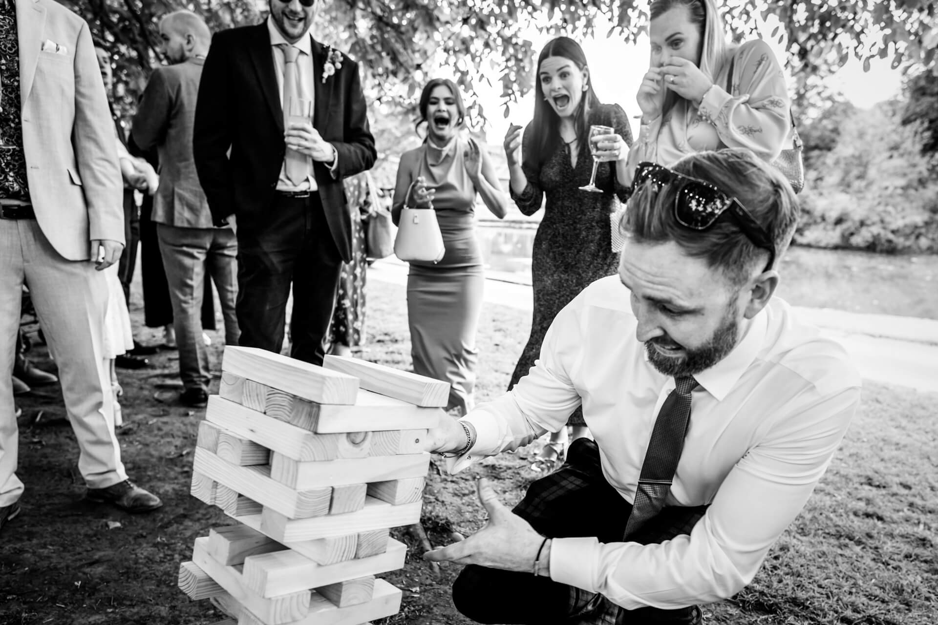 Man playing Jenga at wedding, guests laughing