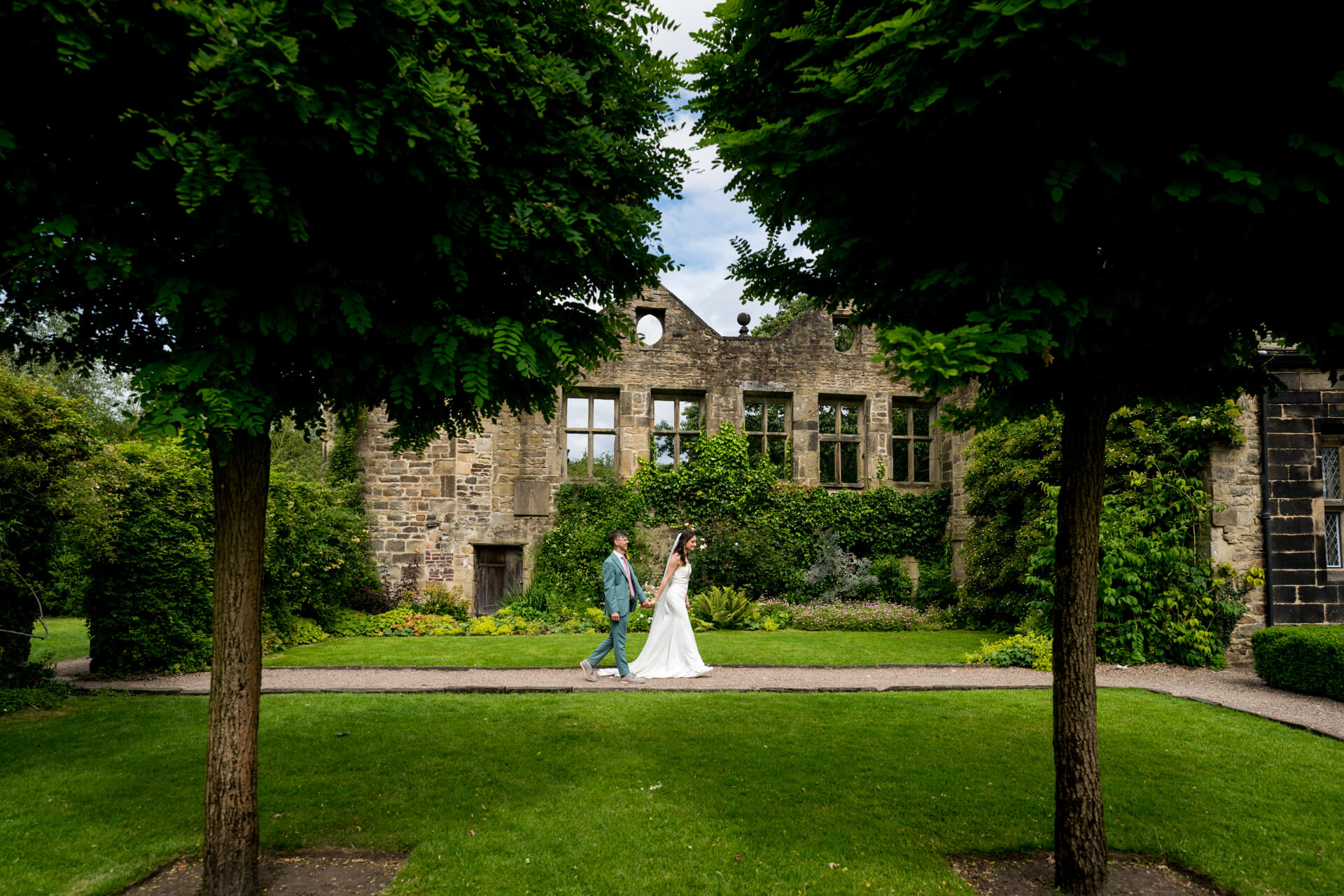 Bride and groom walking by historic stone building at East Riddlesden Hall