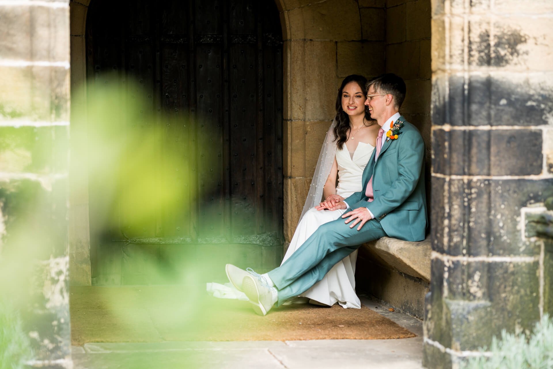 Wedding couple sitting by ancient door, smiling