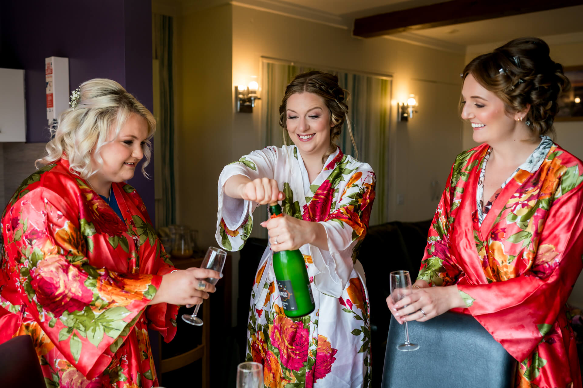 Bride and bridesmaids in floral robes celebrating with champagne