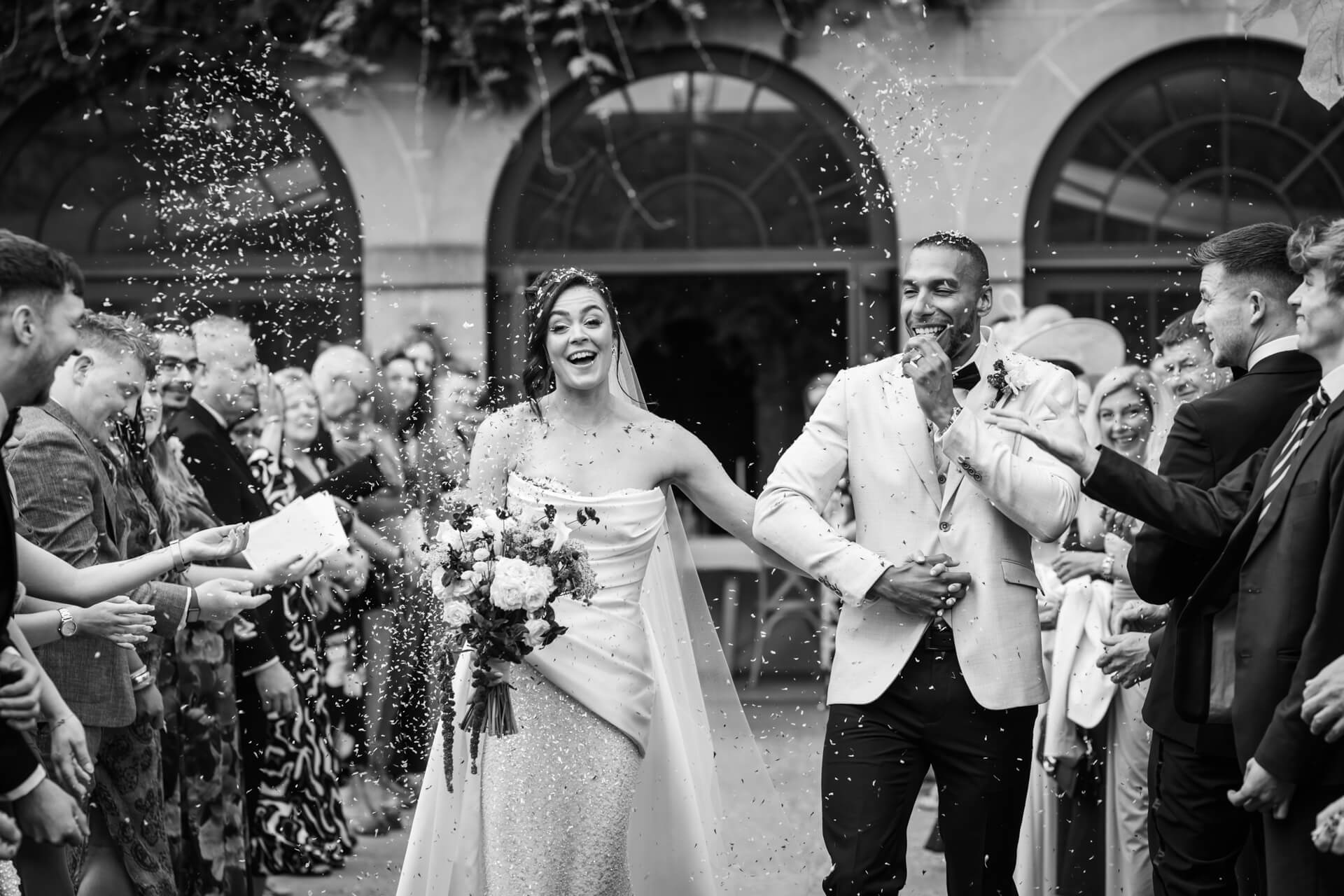 Newlyweds smiling as guests throw confetti.