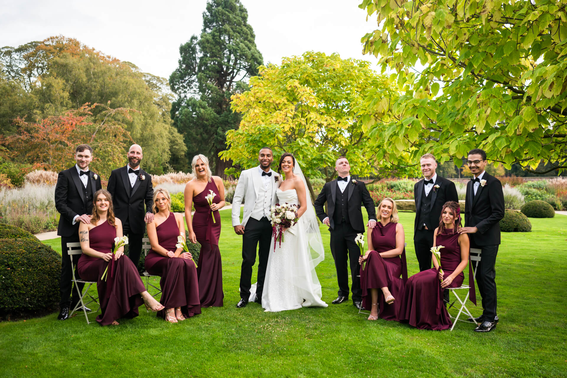 Wedding party posing in garden, smiling happily.