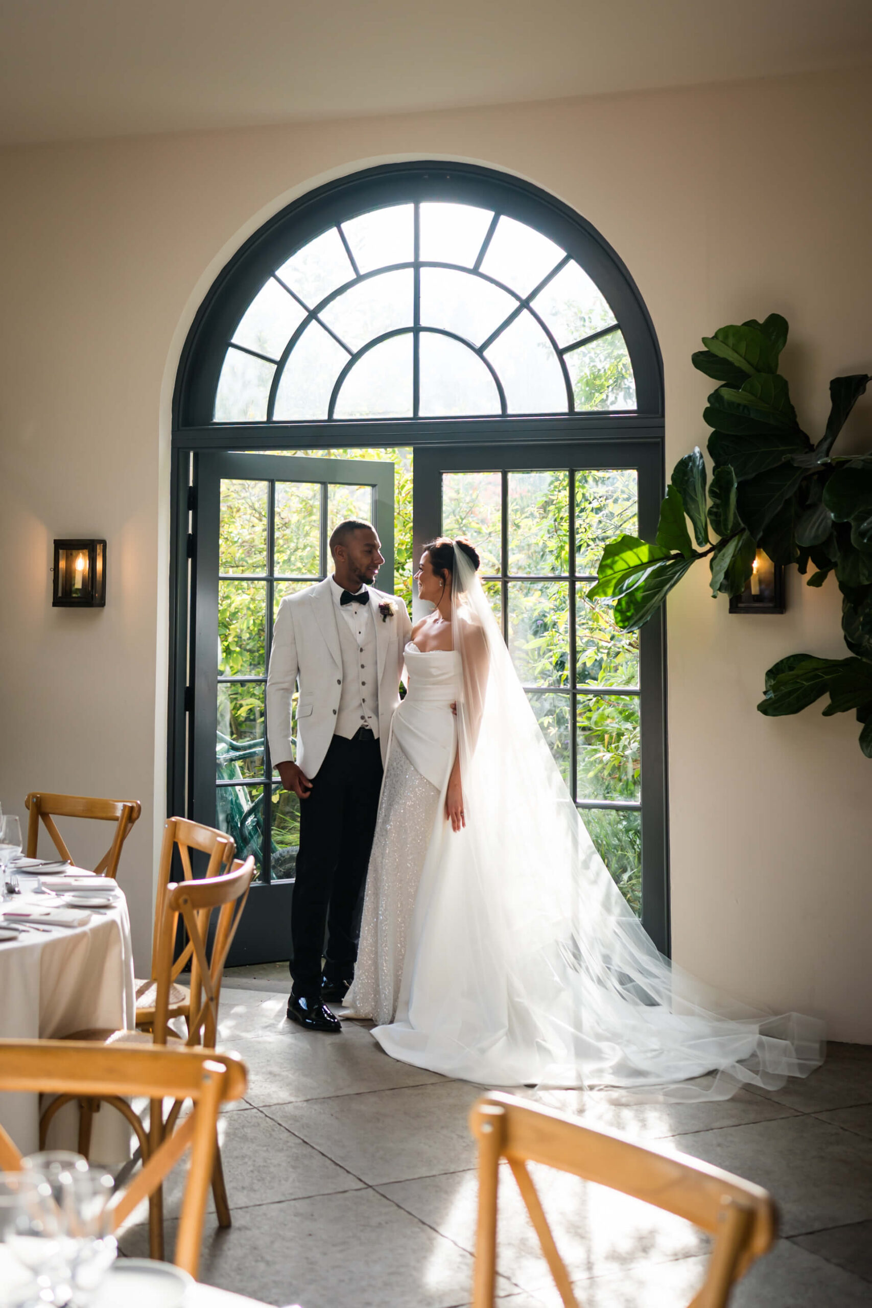Bride and groom standing by large window.