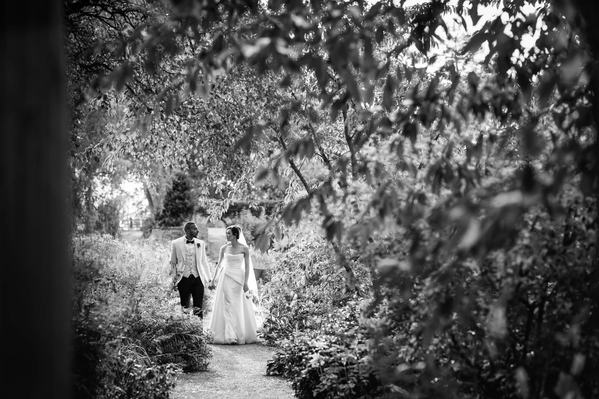 Bride and groom walking in leafy garden path.