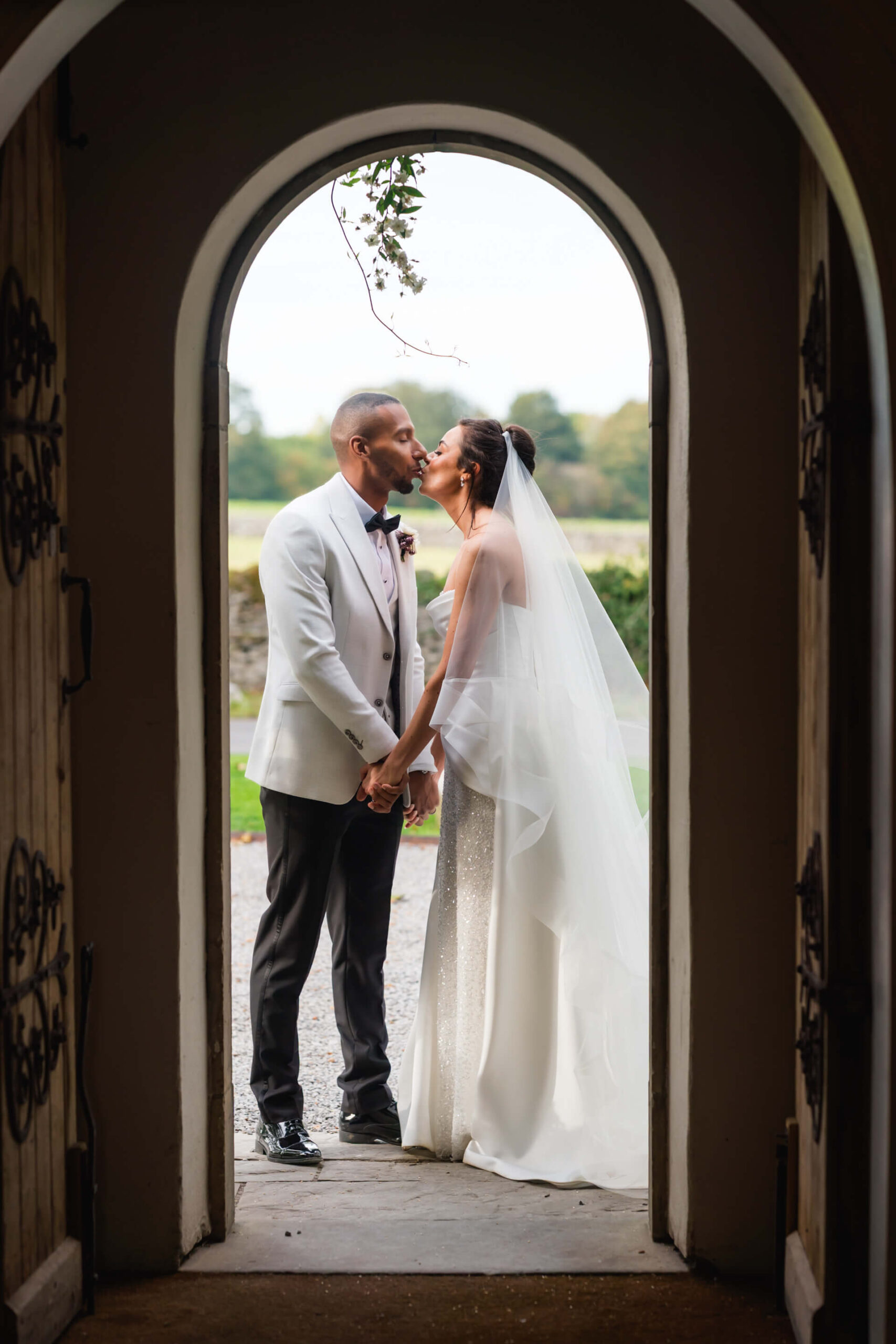 Couple kissing at wedding, framed by arched doorway.