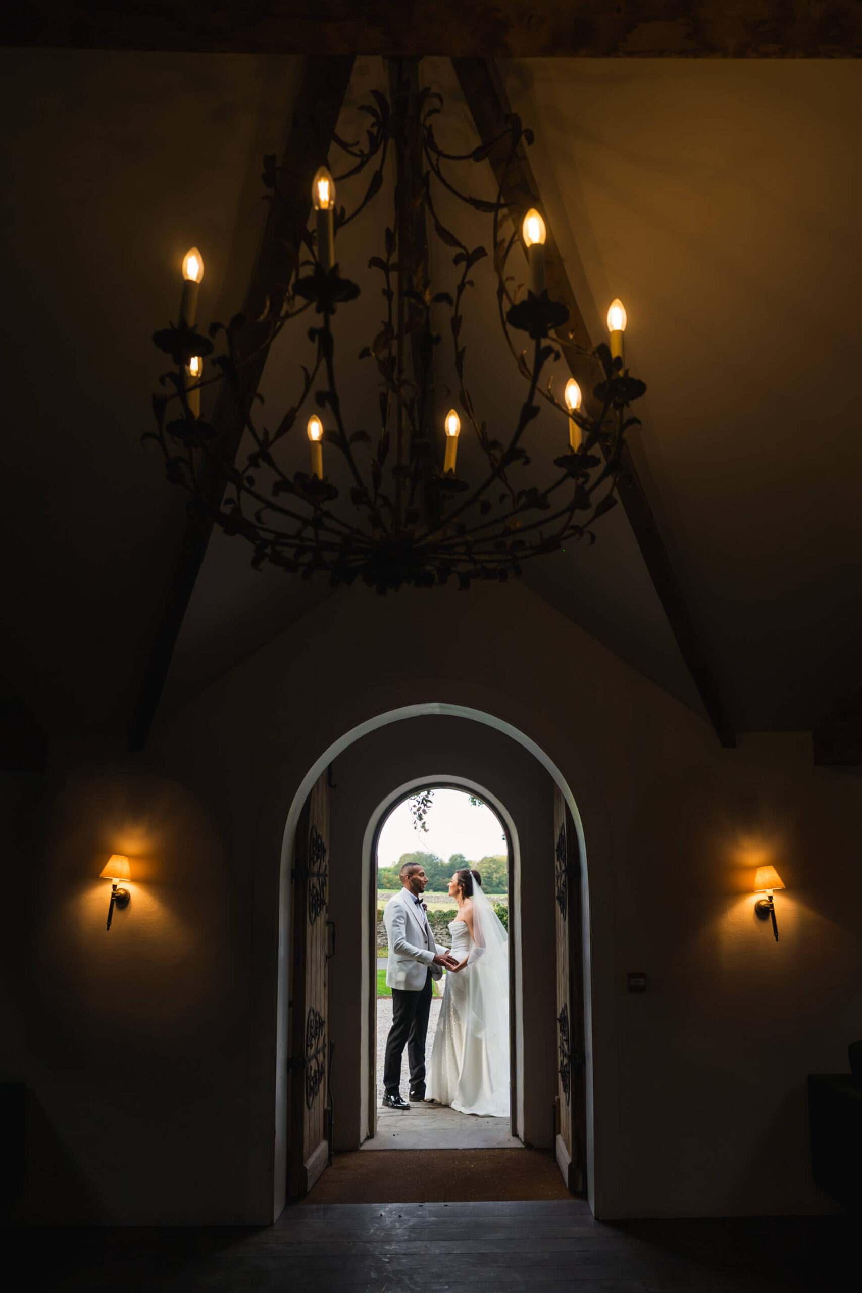 Newlyweds holding hands under arched doorway chandelier.