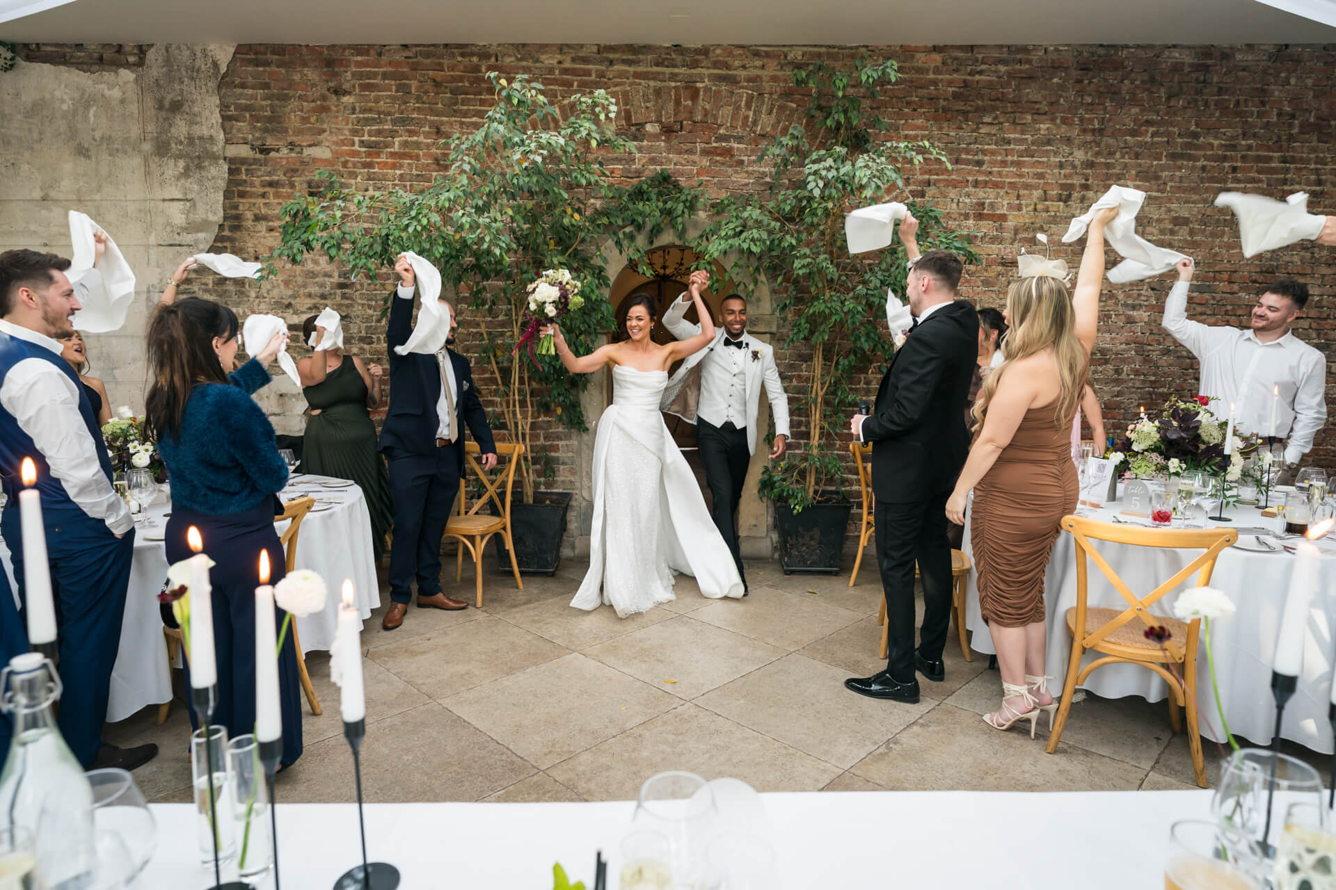 Newlyweds enter wedding reception, guests celebrating.
