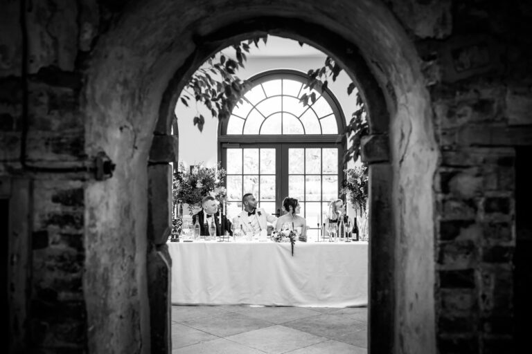 Wedding guests seated through arched brick doorway.