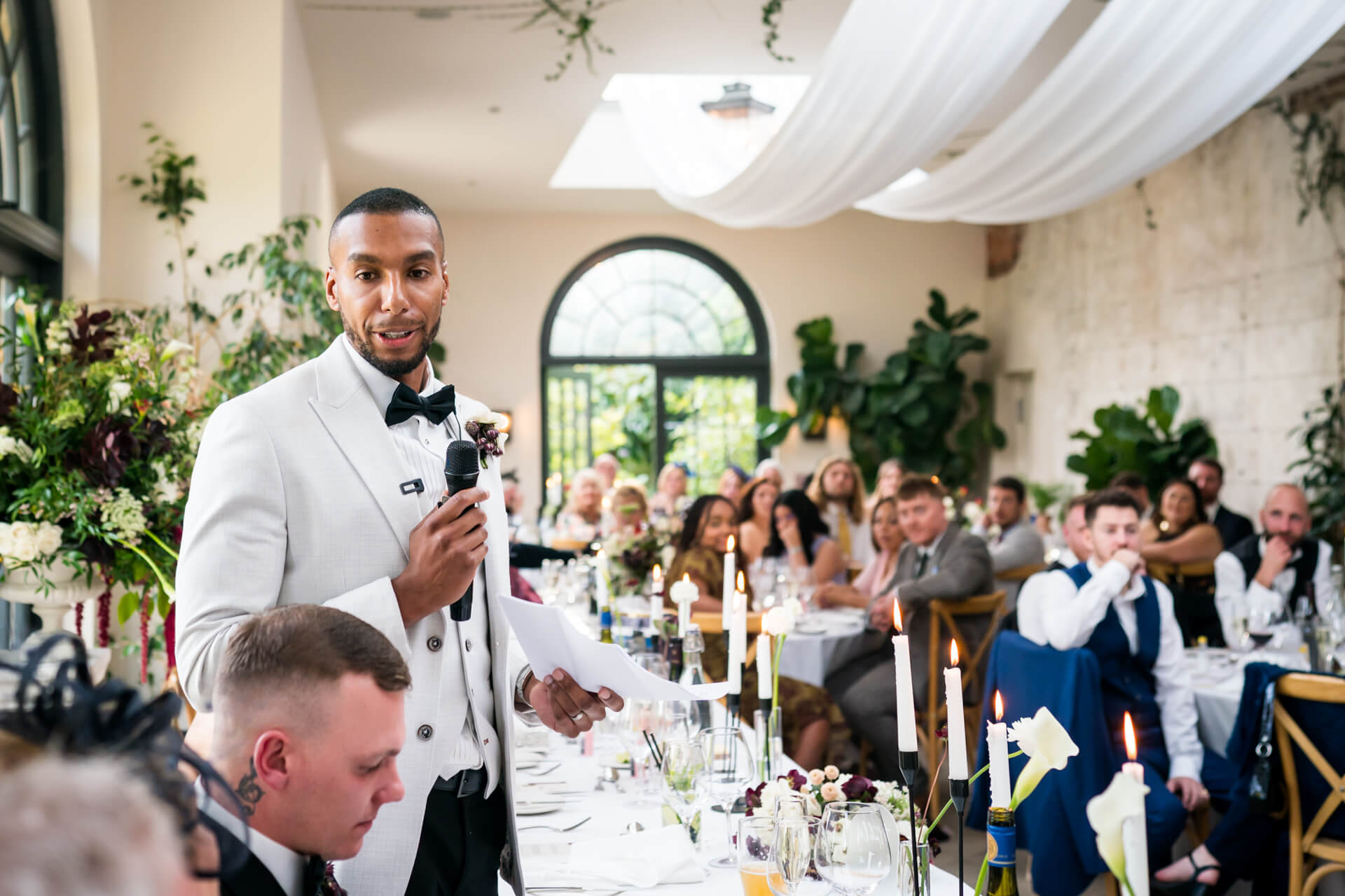Man giving speech at formal event with audience seated.
