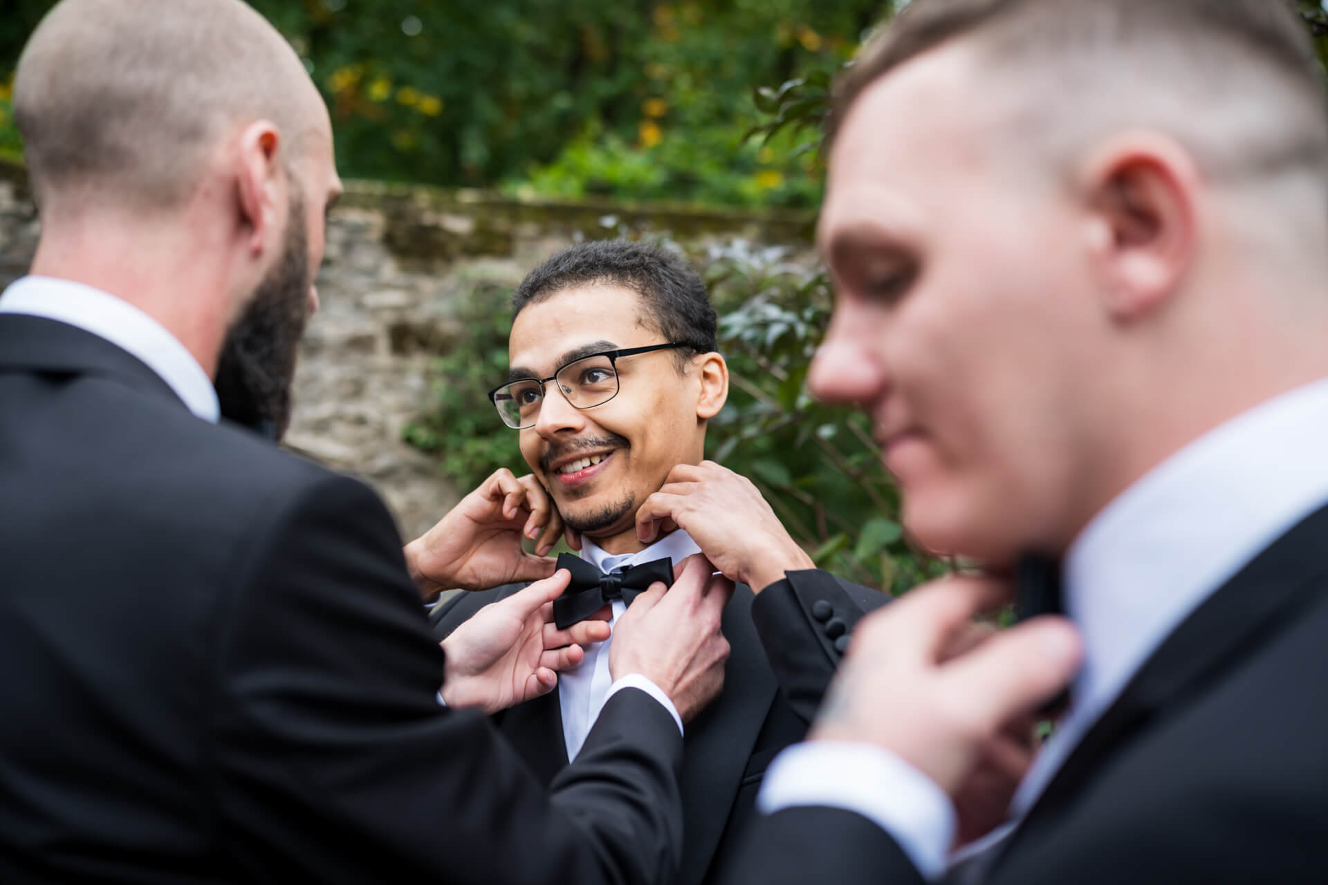 Smiling men adjusting bow tie outdoors.
