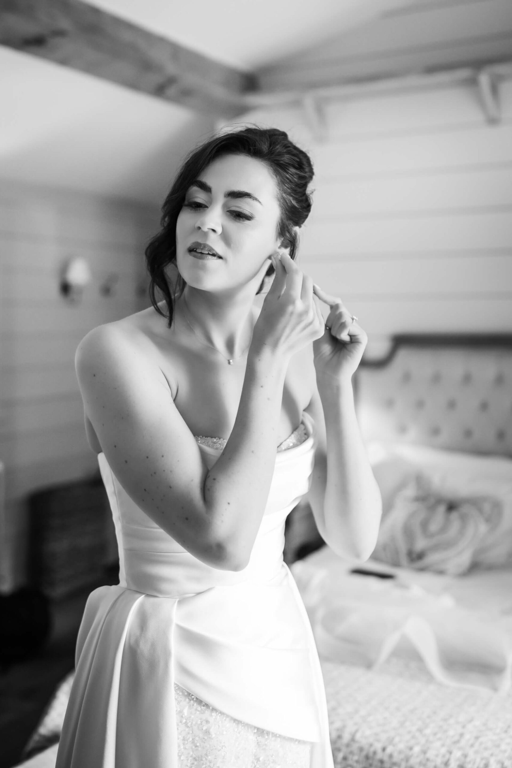 Bride adjusting earrings in bedroom.