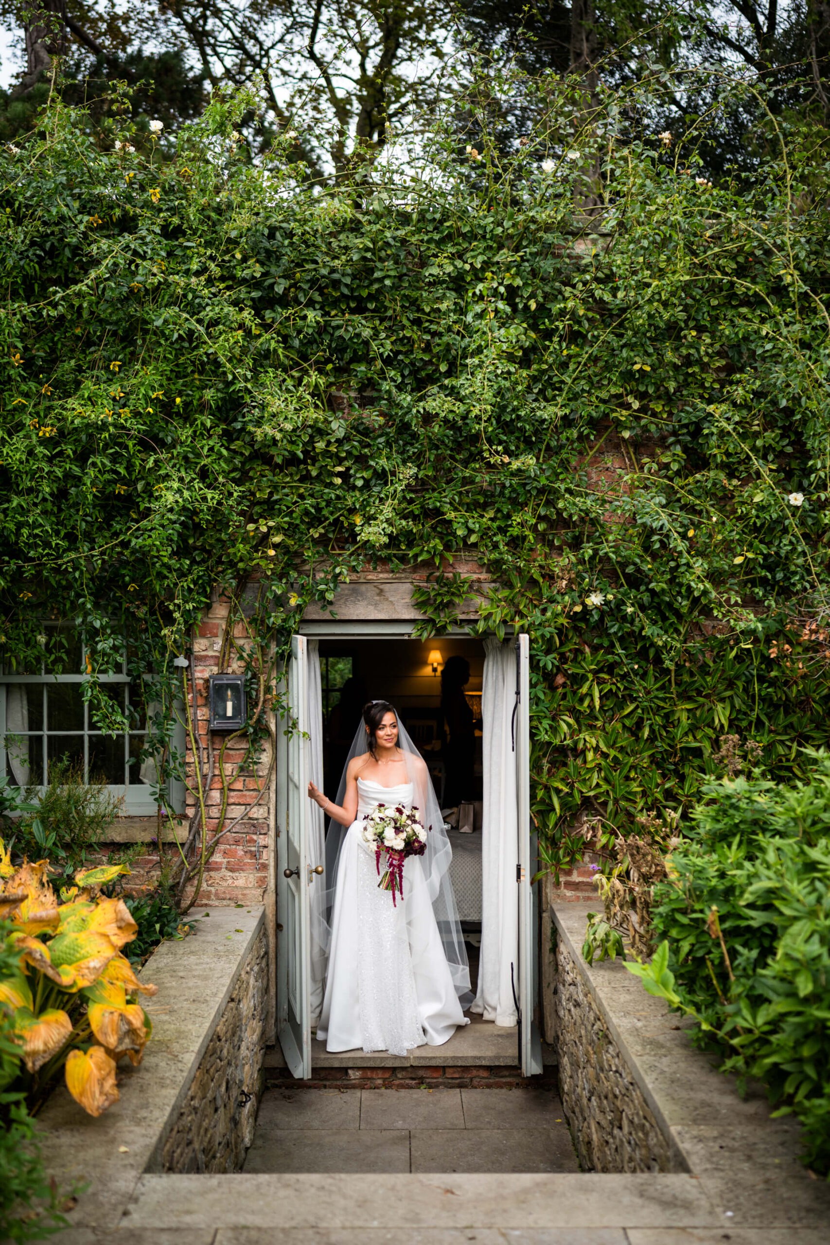 Bride in doorway surrounded by ivy-covered walls.