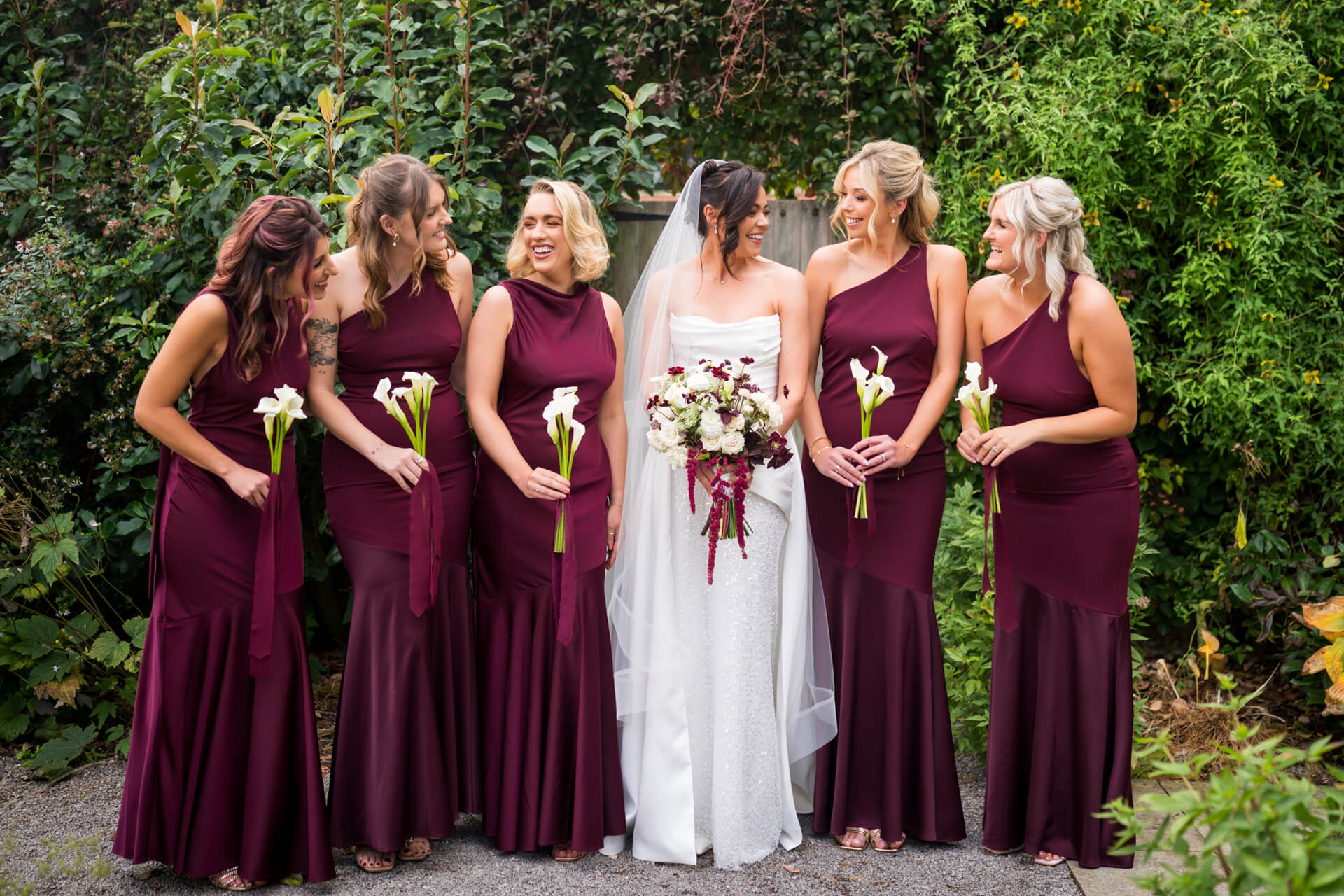 Bride with bridesmaids in burgundy dresses, holding flowers.