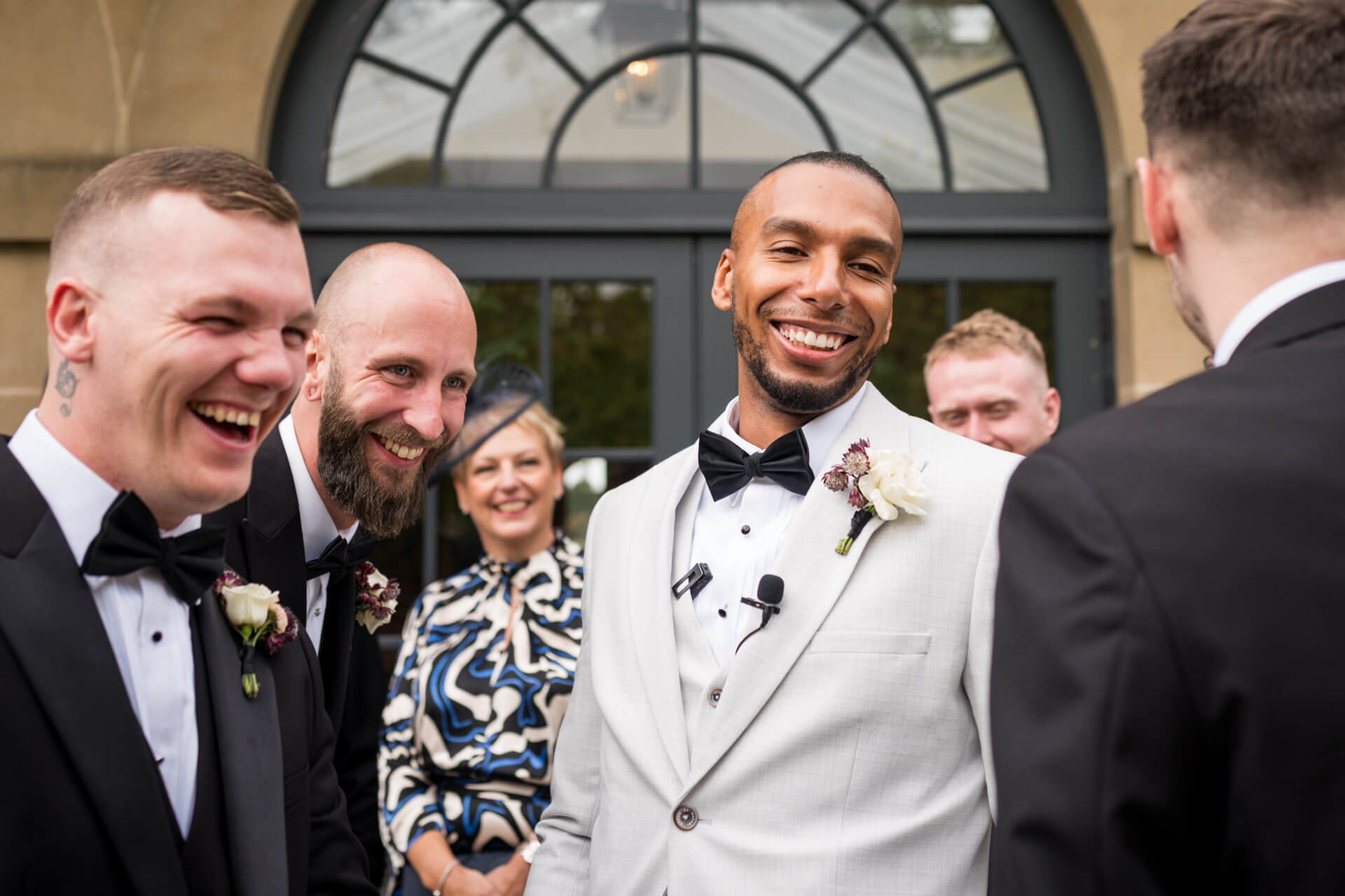 Groomsmen laughing and smiling at wedding ceremony.