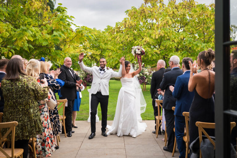 Happy couple walks down wedding aisle, guests applaud.