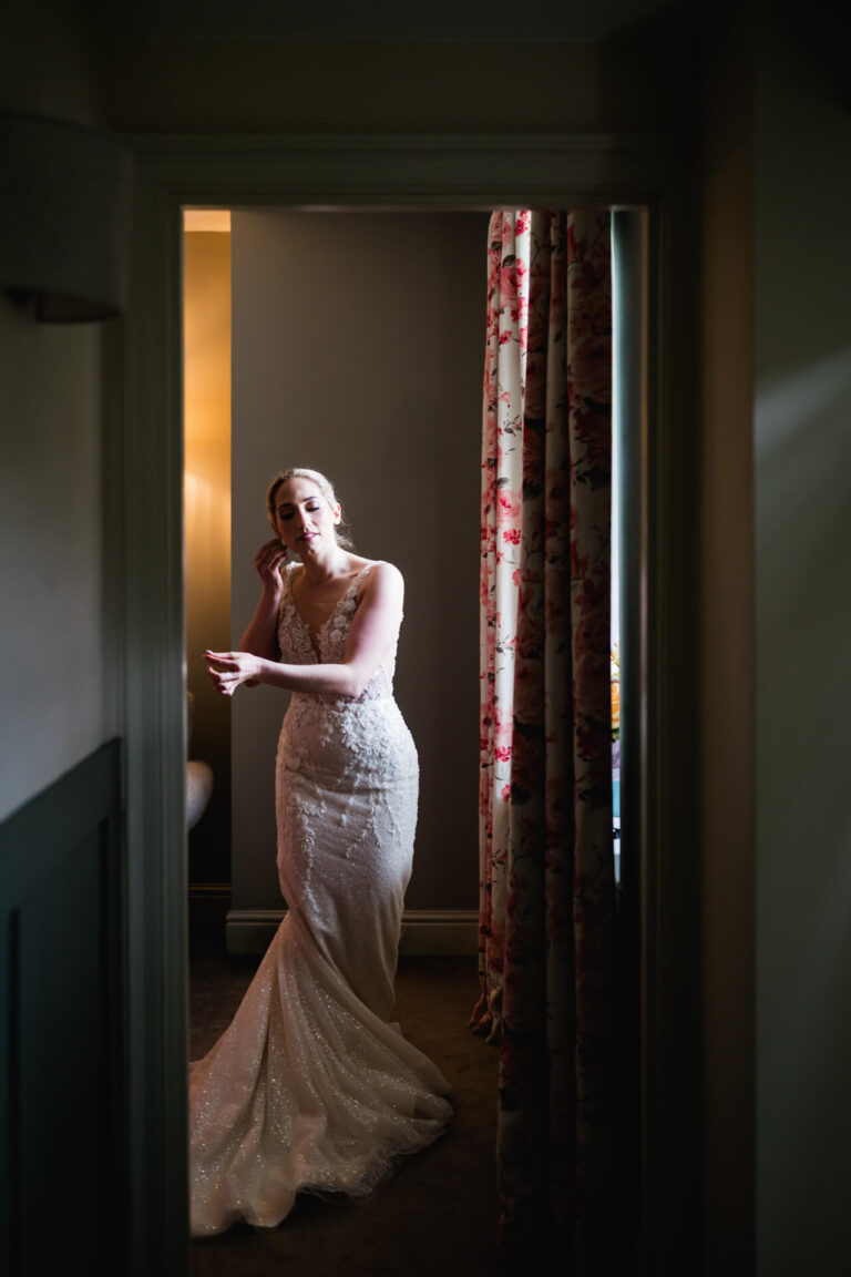 Bride in elegant dress adjusts earring.