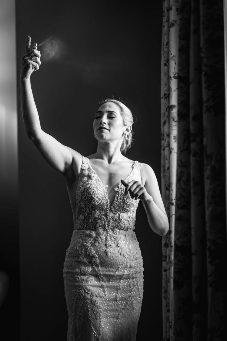 Bride spraying perfume, wearing elegant wedding dress.