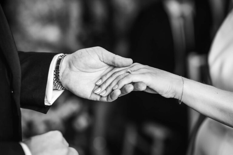 Couple holding hands with engagement ring visible.