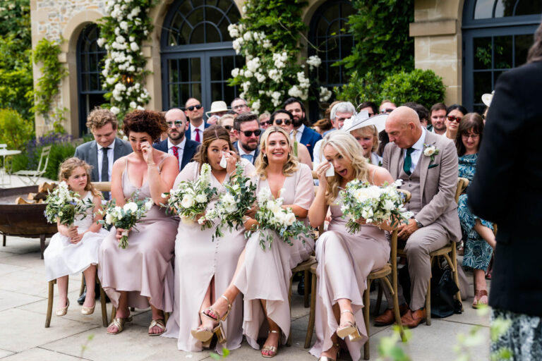 Bridesmaids sitting and wiping tears during wedding ceremony.