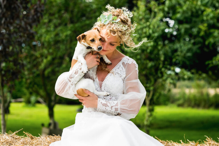 Bride holding dog in garden setting.