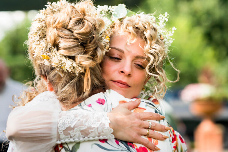 Two women embracing at outdoor wedding ceremony.
